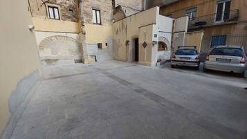 A narrow street with two parked cars, a building with a stone archway, and a small courtyard.