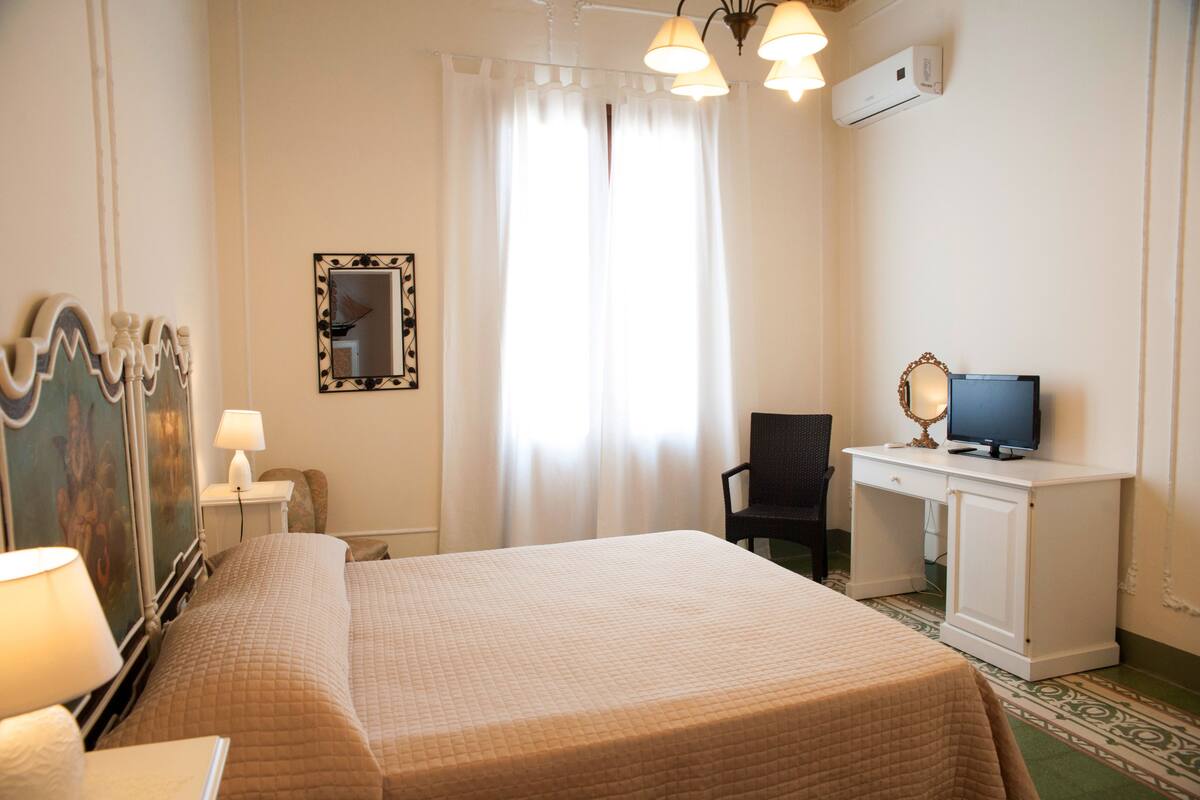 A hotel room with a bed, a desk with a computer, a chair, a mirror, and a window with curtains.