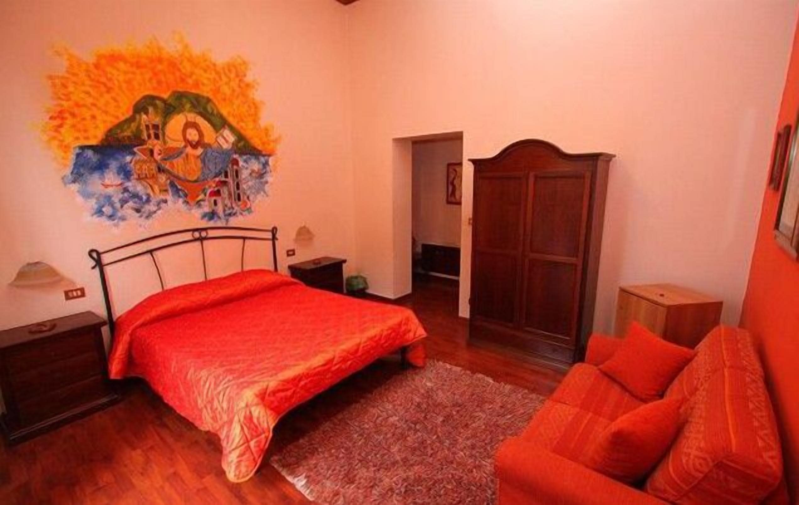 A bedroom with a bed, a wooden wardrobe, a red sofa, and a painting on the wall.