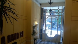 A hallway with a checkered floor, a potted plant, and a wall with framed items. - Hotel Concordia (Palermo)