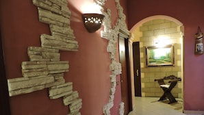 A hallway with a stone wall design, a door, and a framed painting on the wall. - Hotel Concordia (Palermo)