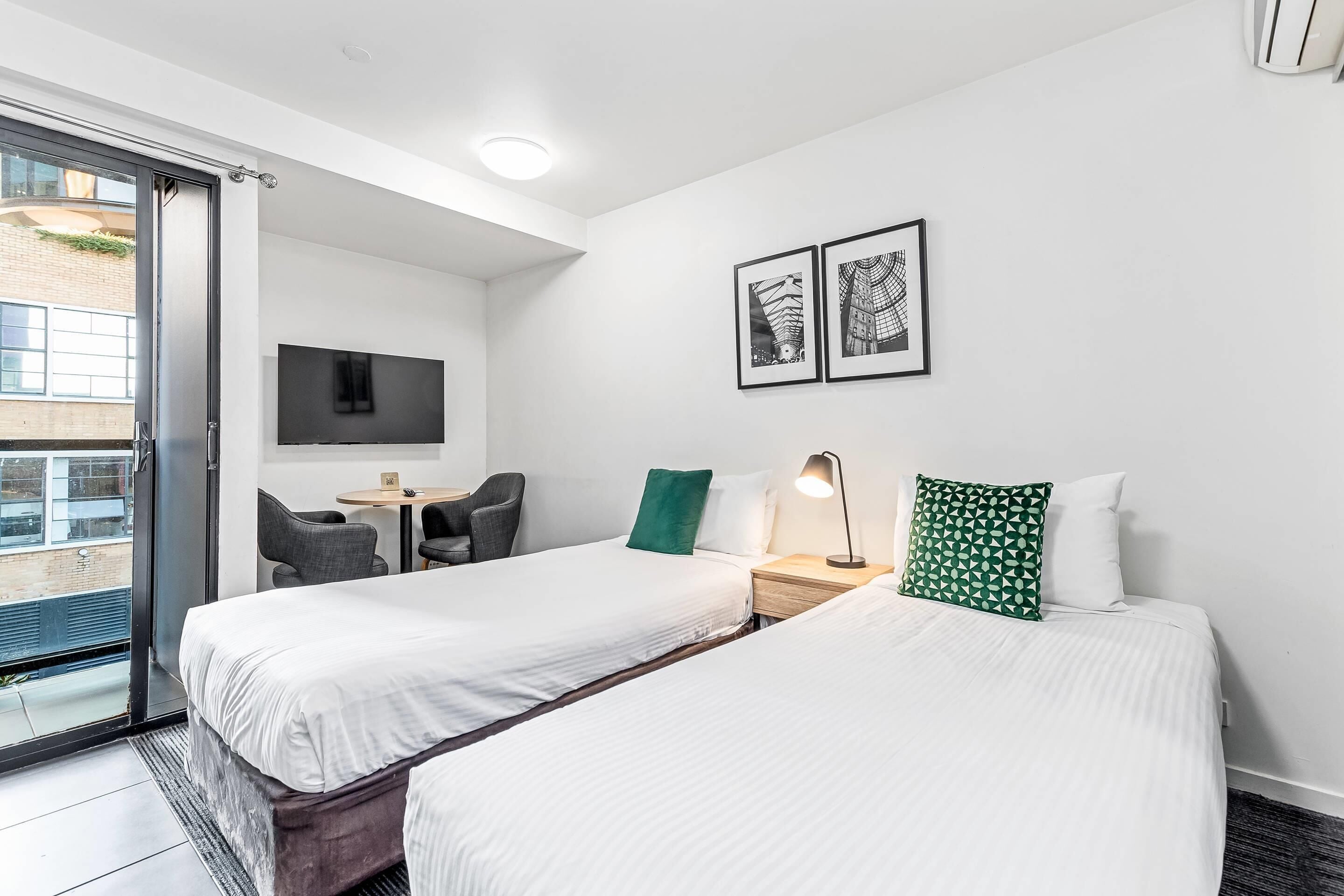 Habitación de hotel con dos camas, un escritorio, una silla, un televisor y un balcón.