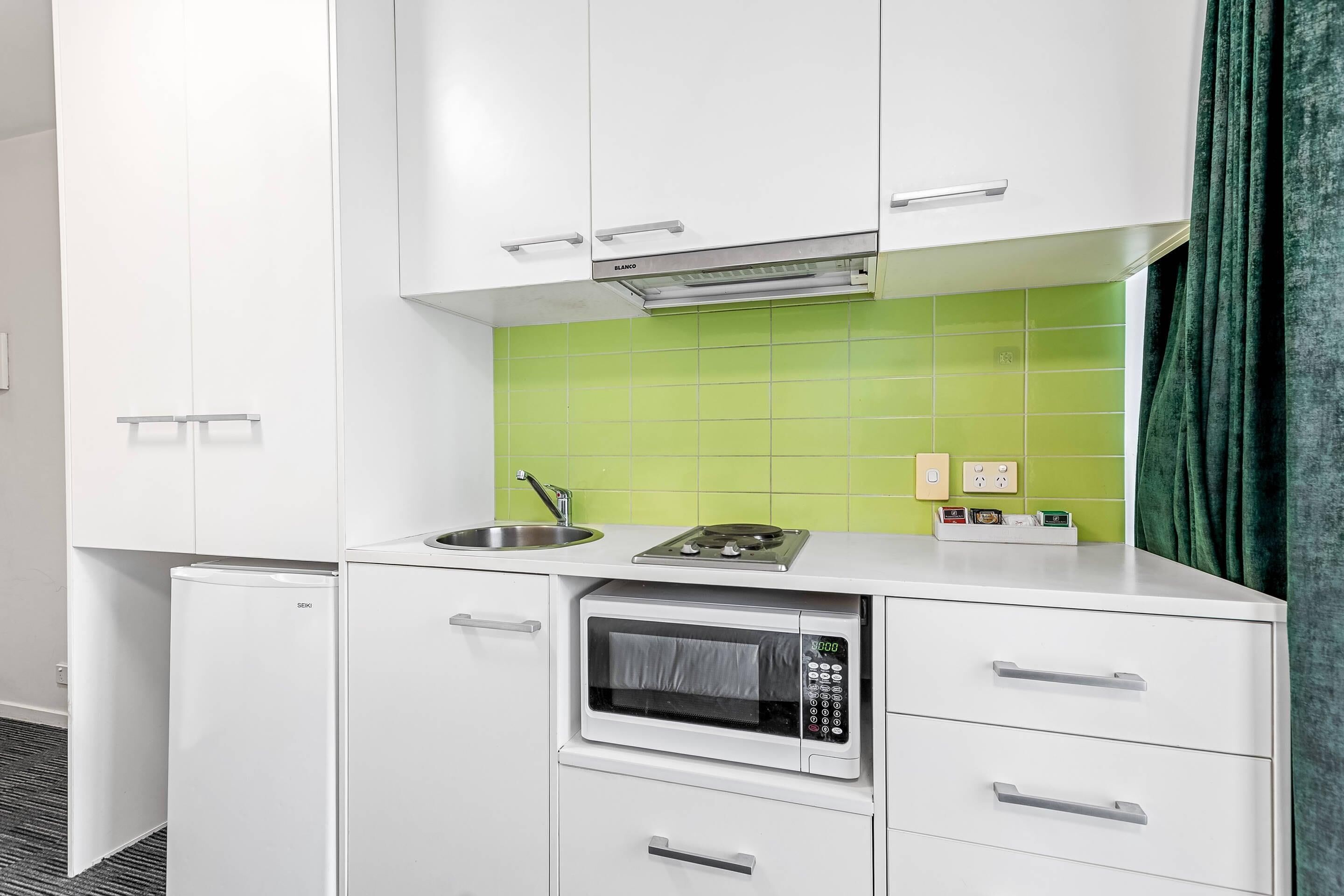 A compact kitchenette with a microwave, stove, and sink.