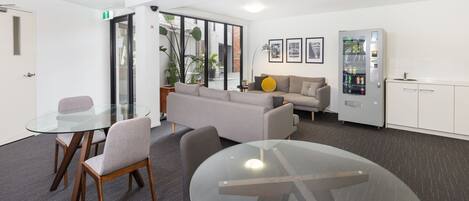 A modern office space with a glass table, two chairs, a sofa, a vending machine, and a cabinet.