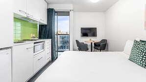 A compact hotel room with a kitchenette, a bed, a small table with two chairs, and a TV mounted on the wall. - Quality Apartments North Melbourne (North Melbourne)