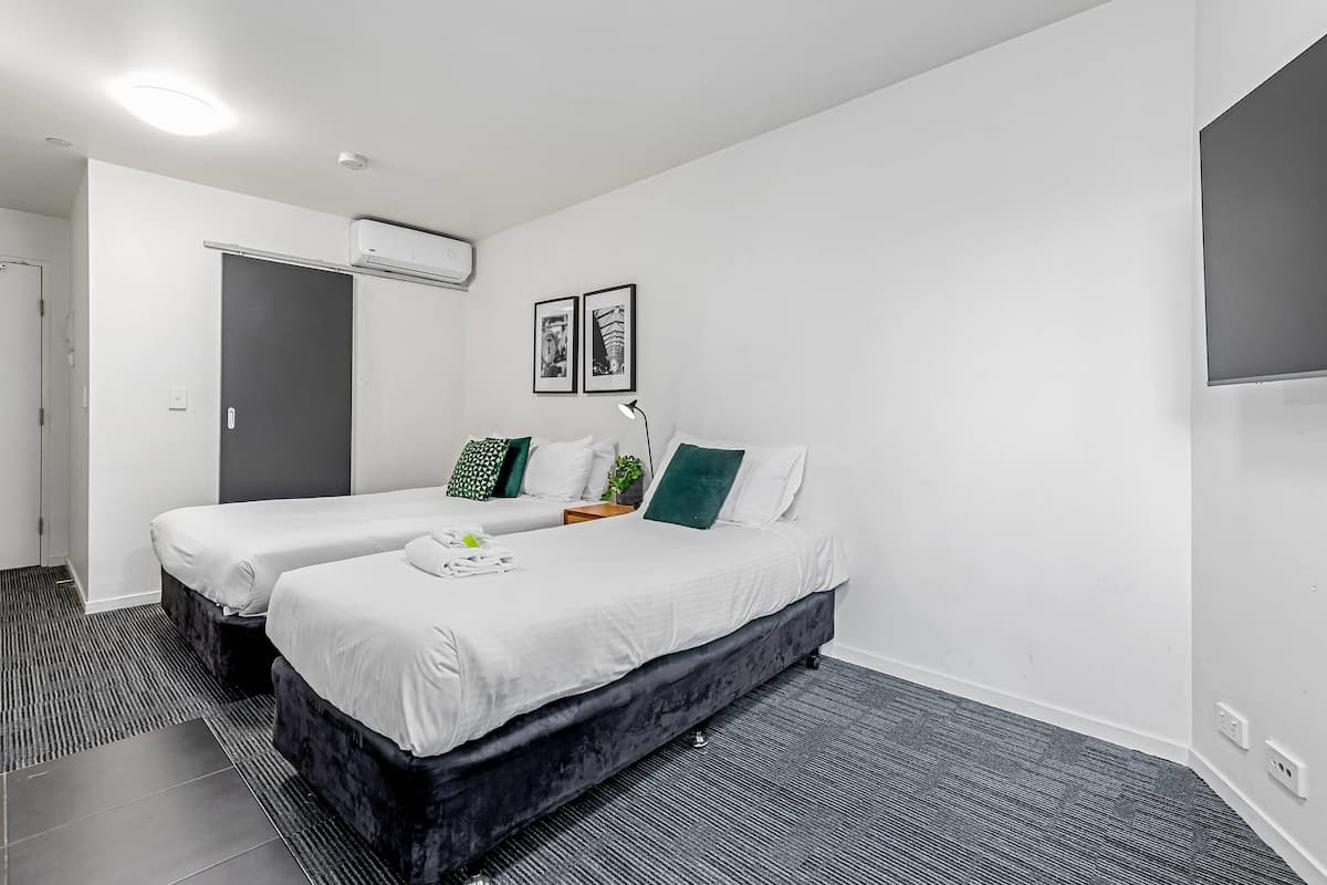 A modern hotel room with two beds, a flat-screen TV, and a small bedside table with a lamp.