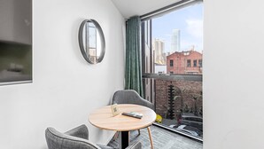 A modern hotel room with a round table, two grey chairs, a small mirror, and a view of the city through large windows. - Quality Apartments North Melbourne (North Melbourne)