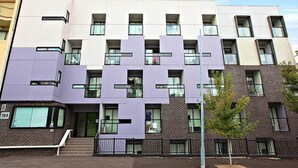 A multi-story building with a modern architectural design, featuring a mix of brick and light-colored facades, and a visible entrance with steps leading up to it. - Quality Apartments North Melbourne (North Melbourne)