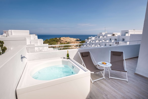 A rooftop terrace with a hot tub, lounge chairs, and a table with a bottle and fruits.