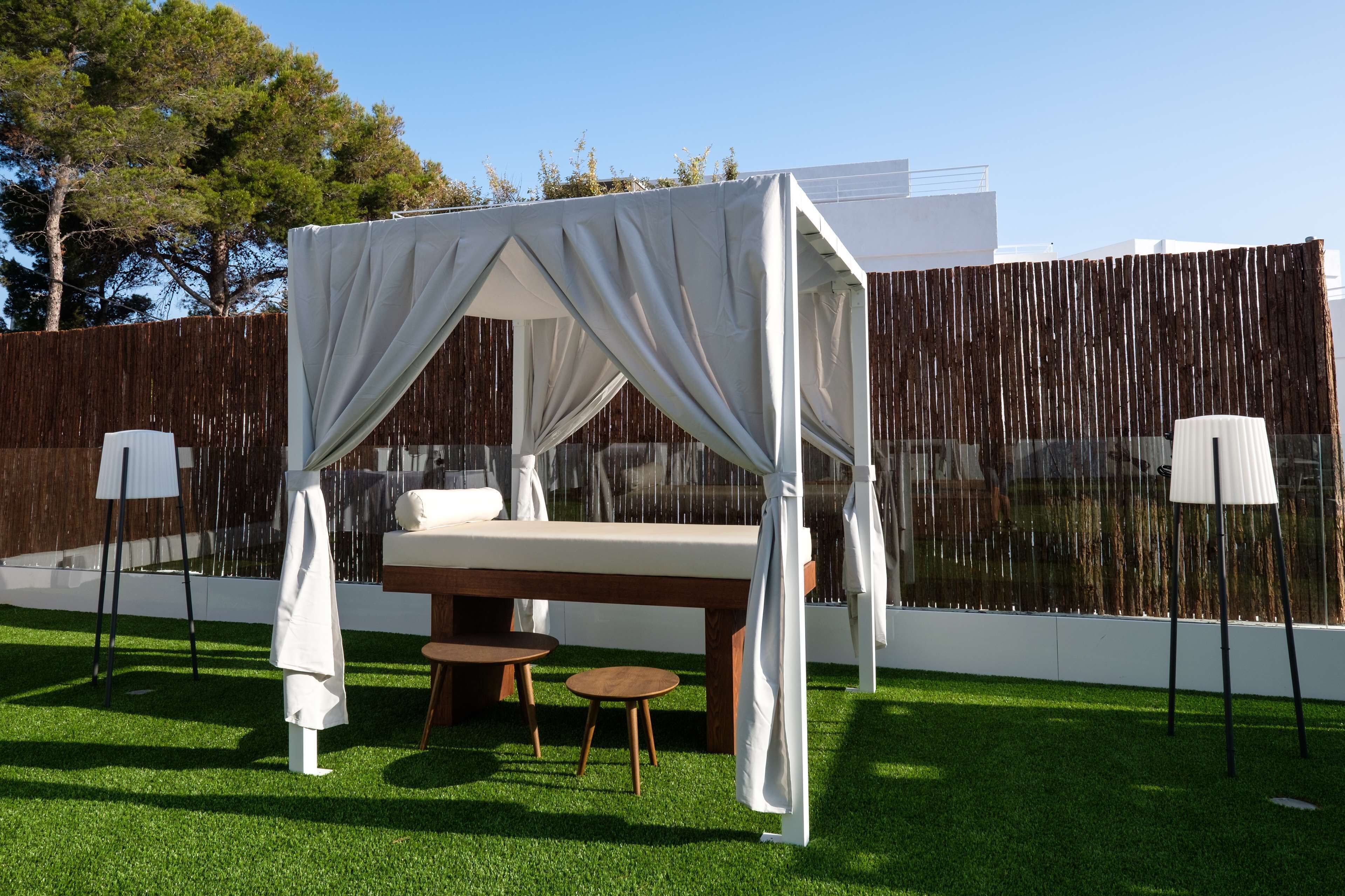 Un espacio exterior privado con una cama con dosel, dos mesitas y un banco.