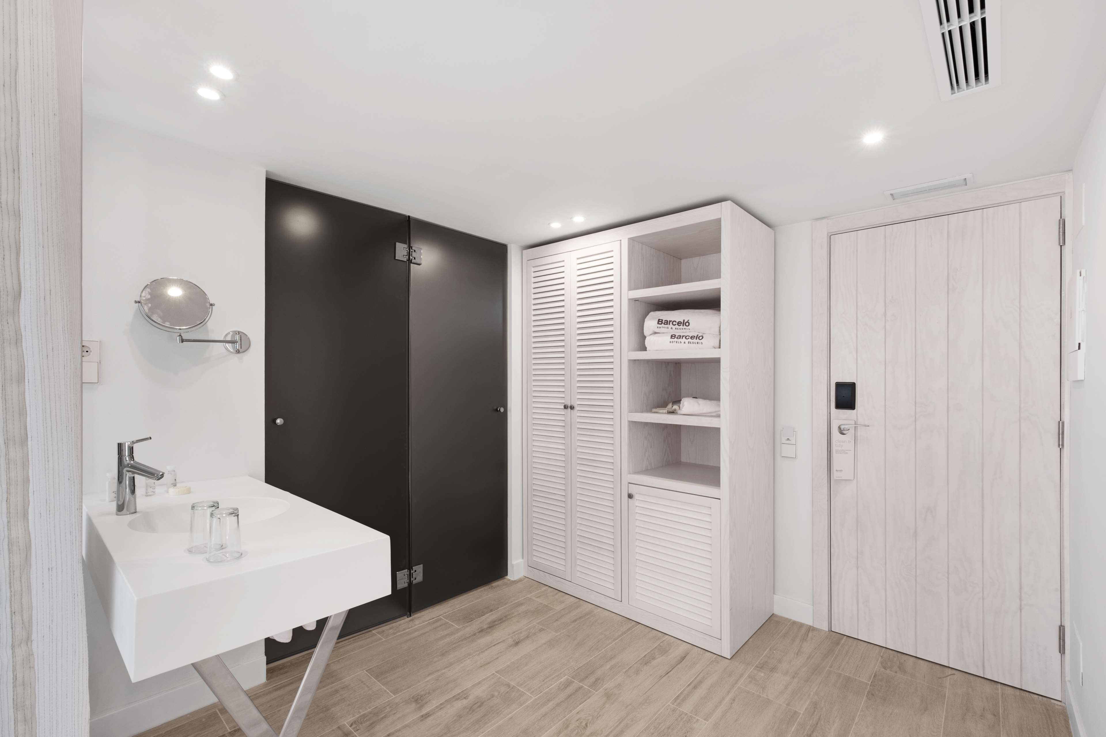 Un baño moderno con un lavabo blanco, una puerta negra y un armario blanco con estantes.