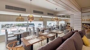 Un espace de restauration moderne avec des chaises et des tables à motifs, de grandes fenêtres offrant une vue sur l’extérieur et un éclairage suspendu.