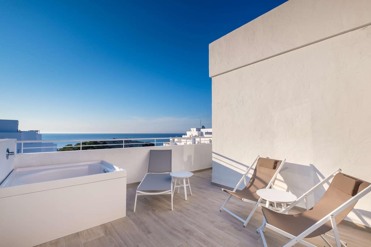 Eine Dachterrasse mit Meerblick, einer Badewanne und zwei Liegestühlen.