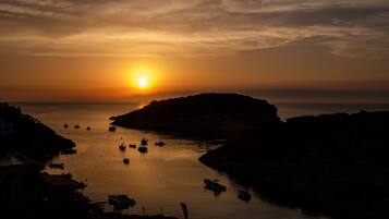 Vista de un atardecer costero con barcos y terreno rocoso.