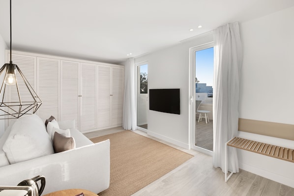 Una sala de estar moderna con sofá, televisión y puerta corrediza de vidrio que da a un balcón.