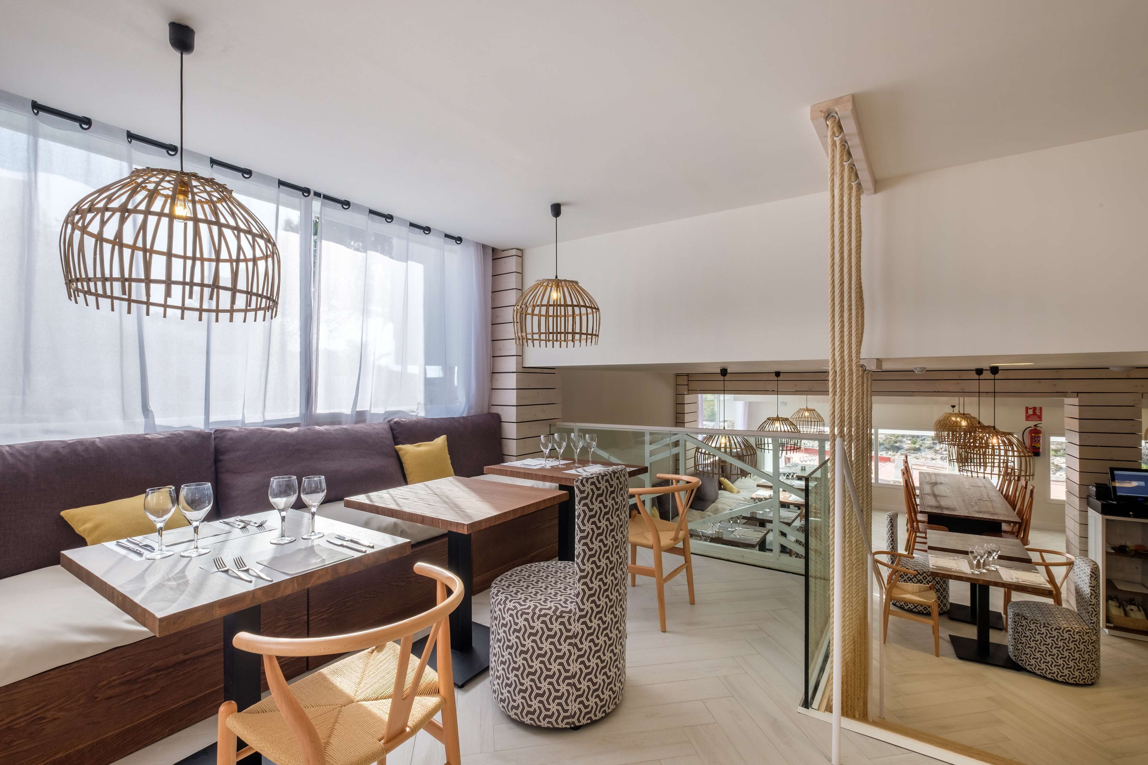 A modern dining area with wooden tables, cushioned seating, and pendant lighting.