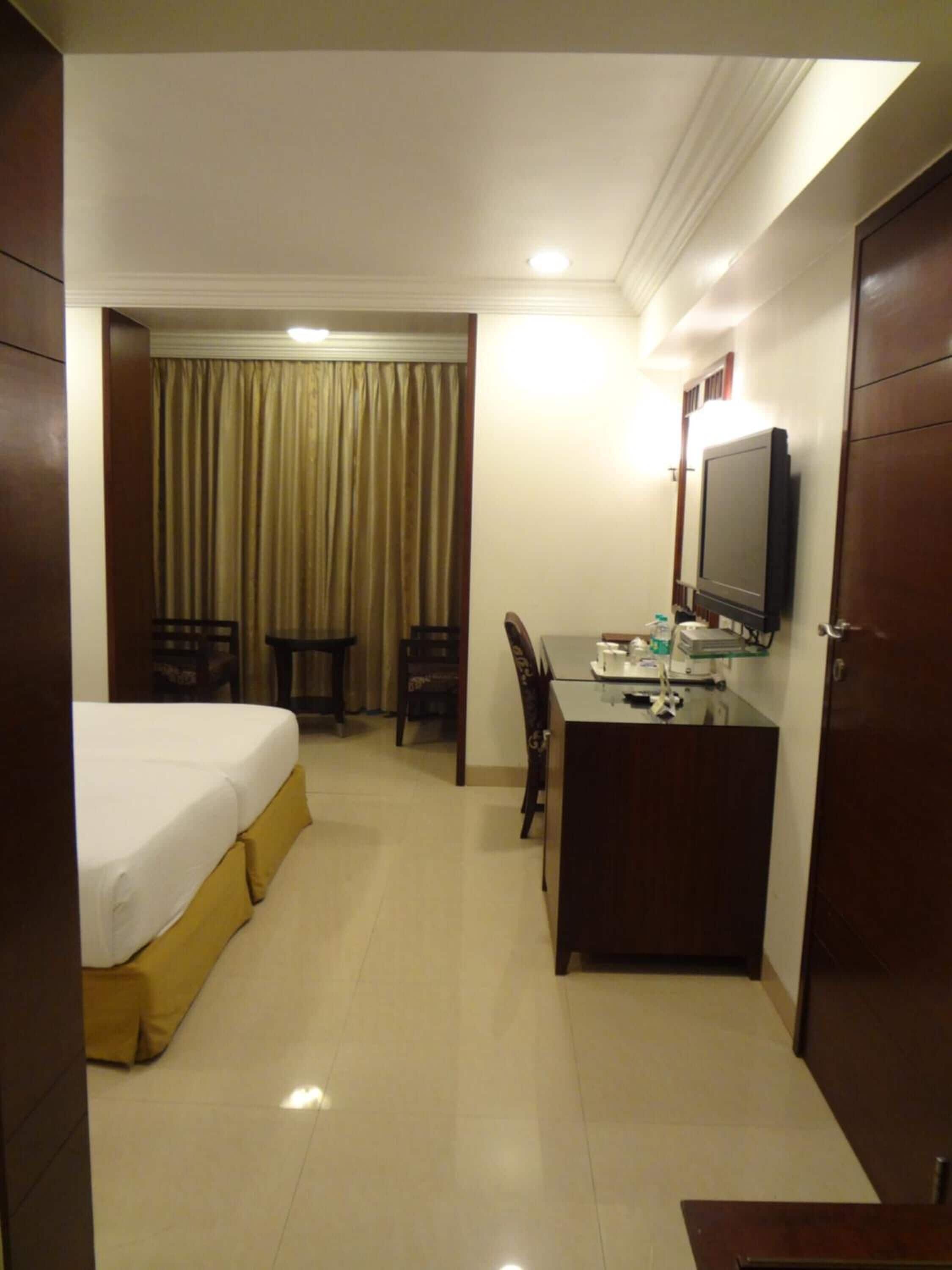A hotel room with a bed, a desk, a chair, a television, and a curtain.
