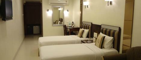 A hotel room with two single beds, a desk with a chair, a mirror, and an air conditioning unit.