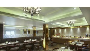 A modern restaurant with high ceilings, chandeliers, and a central bar area. - Hotel Suba Palace (Mumbai)