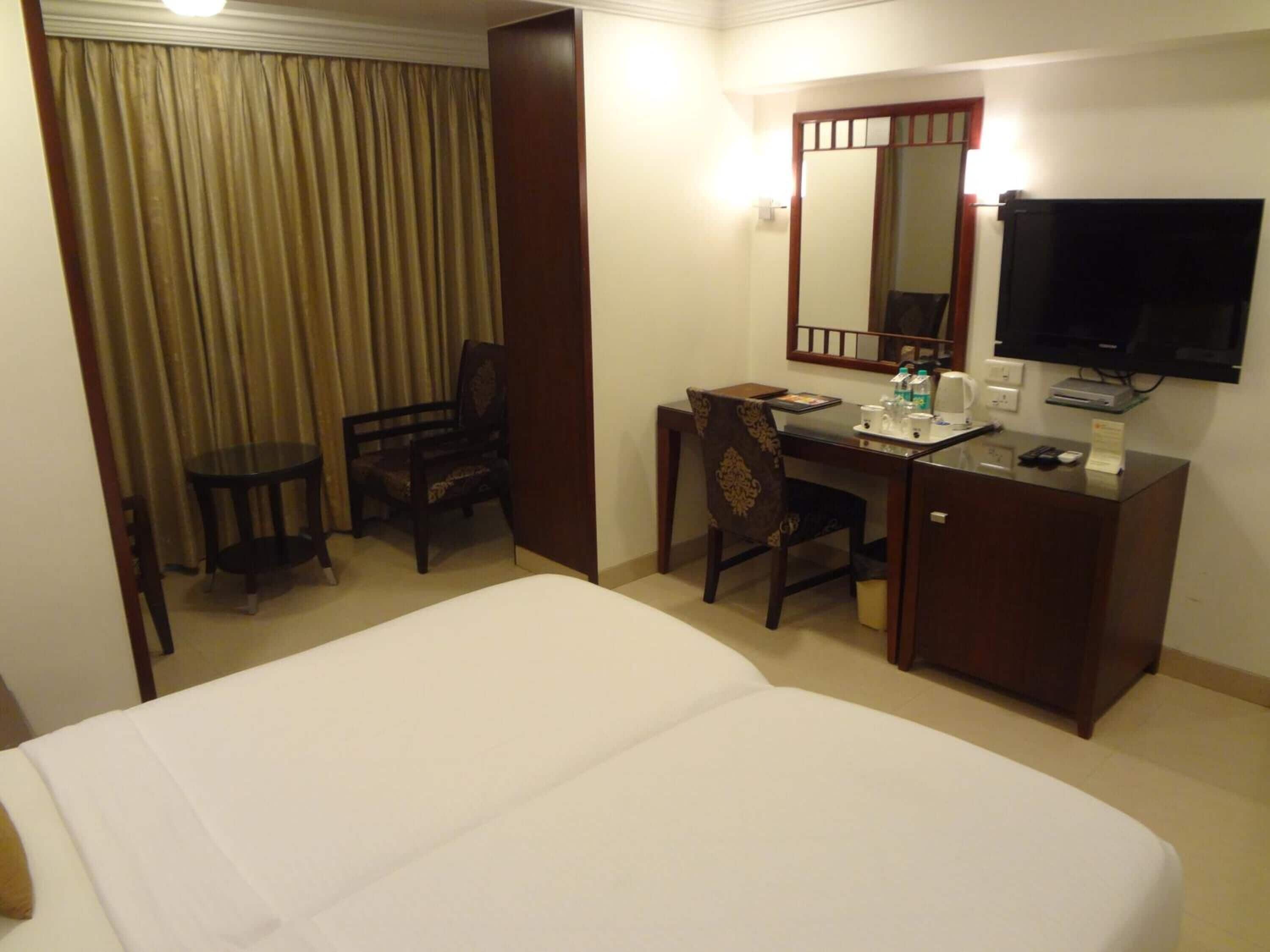 A hotel room with a bed, a desk, a chair, a television, and a mirror.