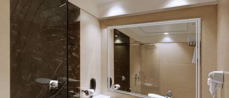 A modern bathroom with a glass shower enclosure, a large mirror, a sink, and a hairdryer on the wall.