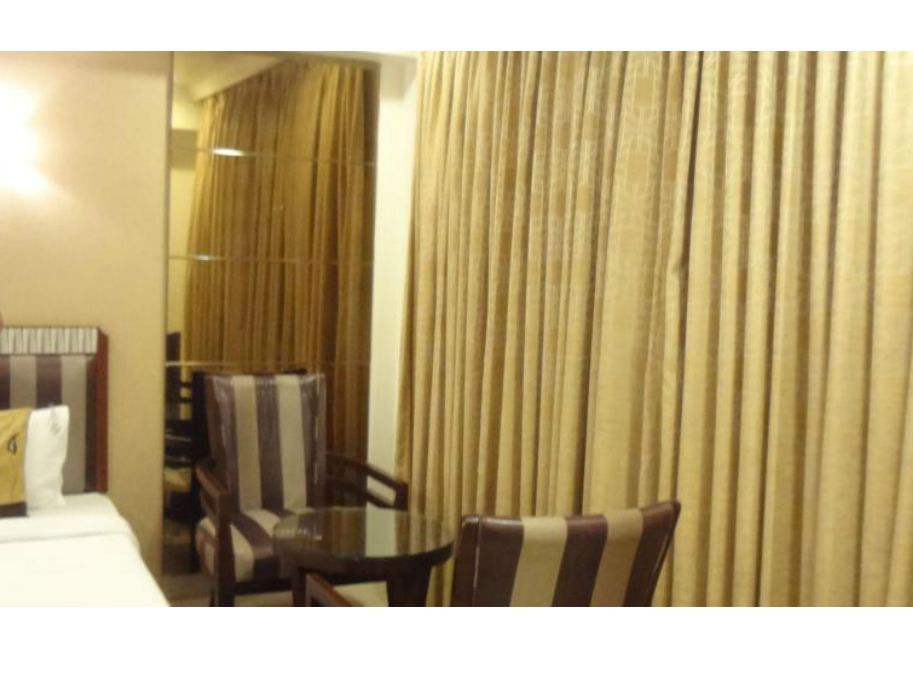 A hotel room with a dining area featuring a table and chairs, a mirror, and a curtain.