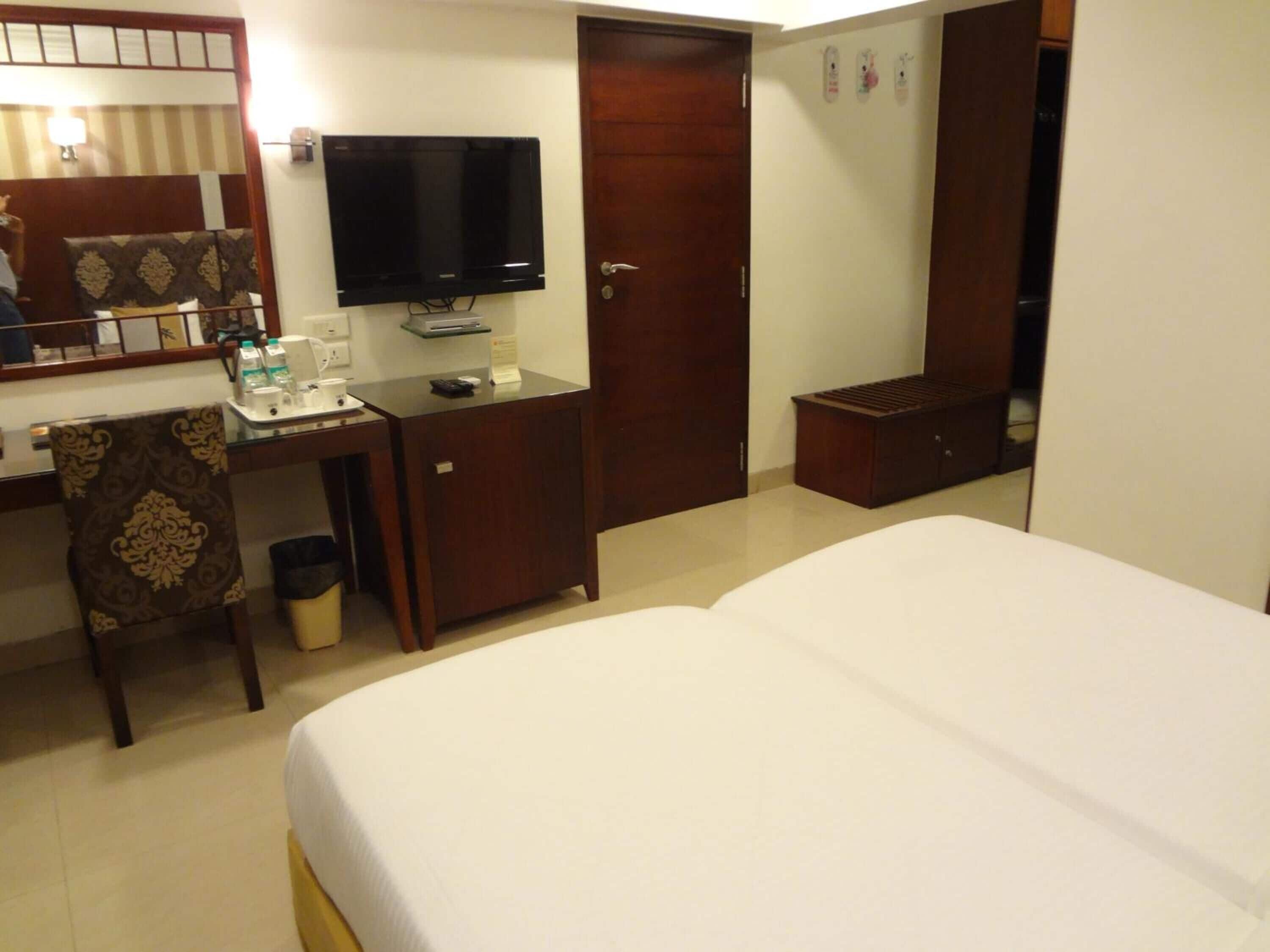 A hotel room with a bed, a desk with a computer, a television, and a wardrobe.