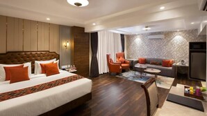 A hotel room with a large bed, a sofa, a chair, a small table, and an air conditioning unit. - Hotel Suba Palace (Mumbai)