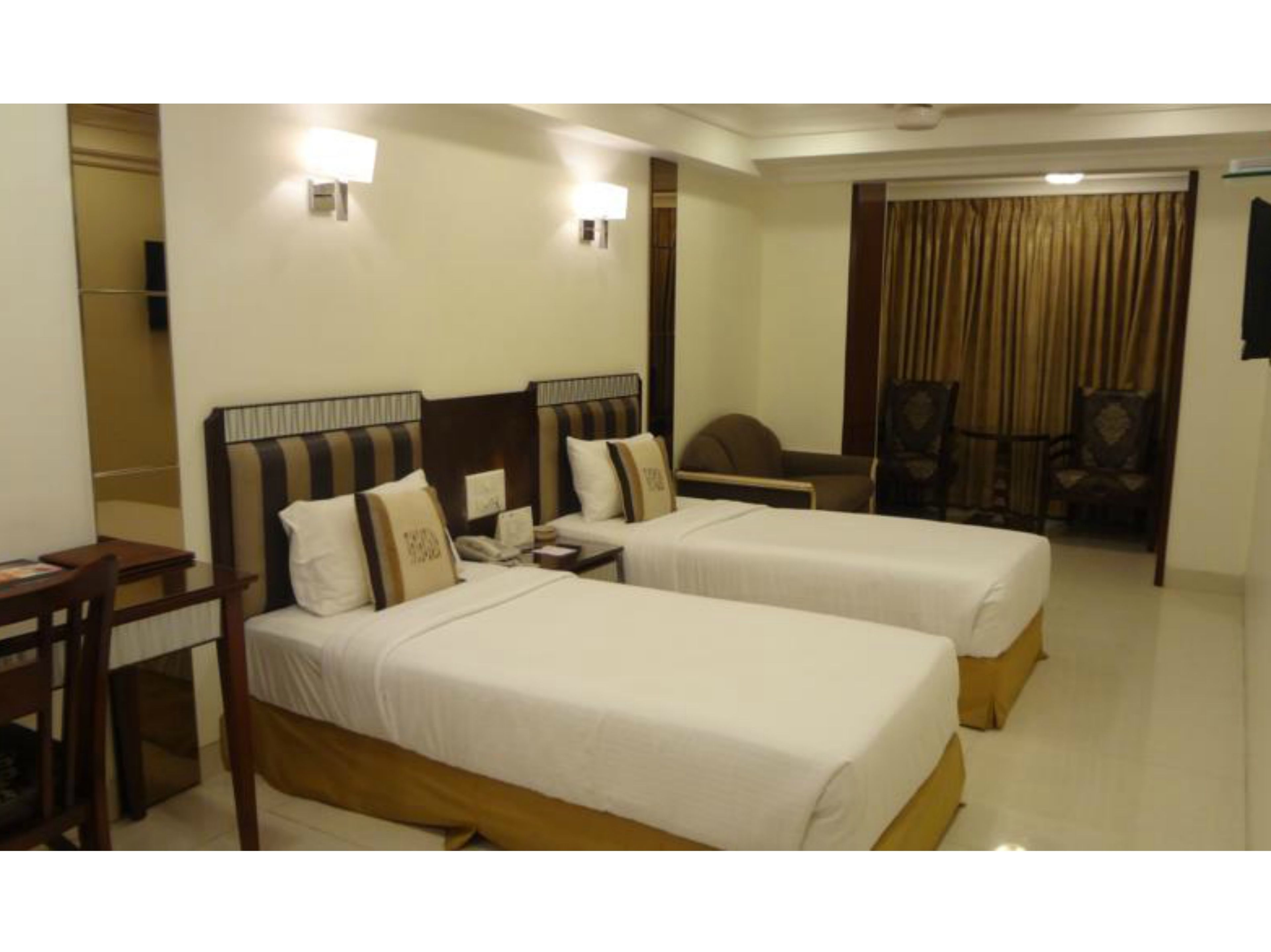A hotel room with two single beds, a desk, a chair, and a small table.