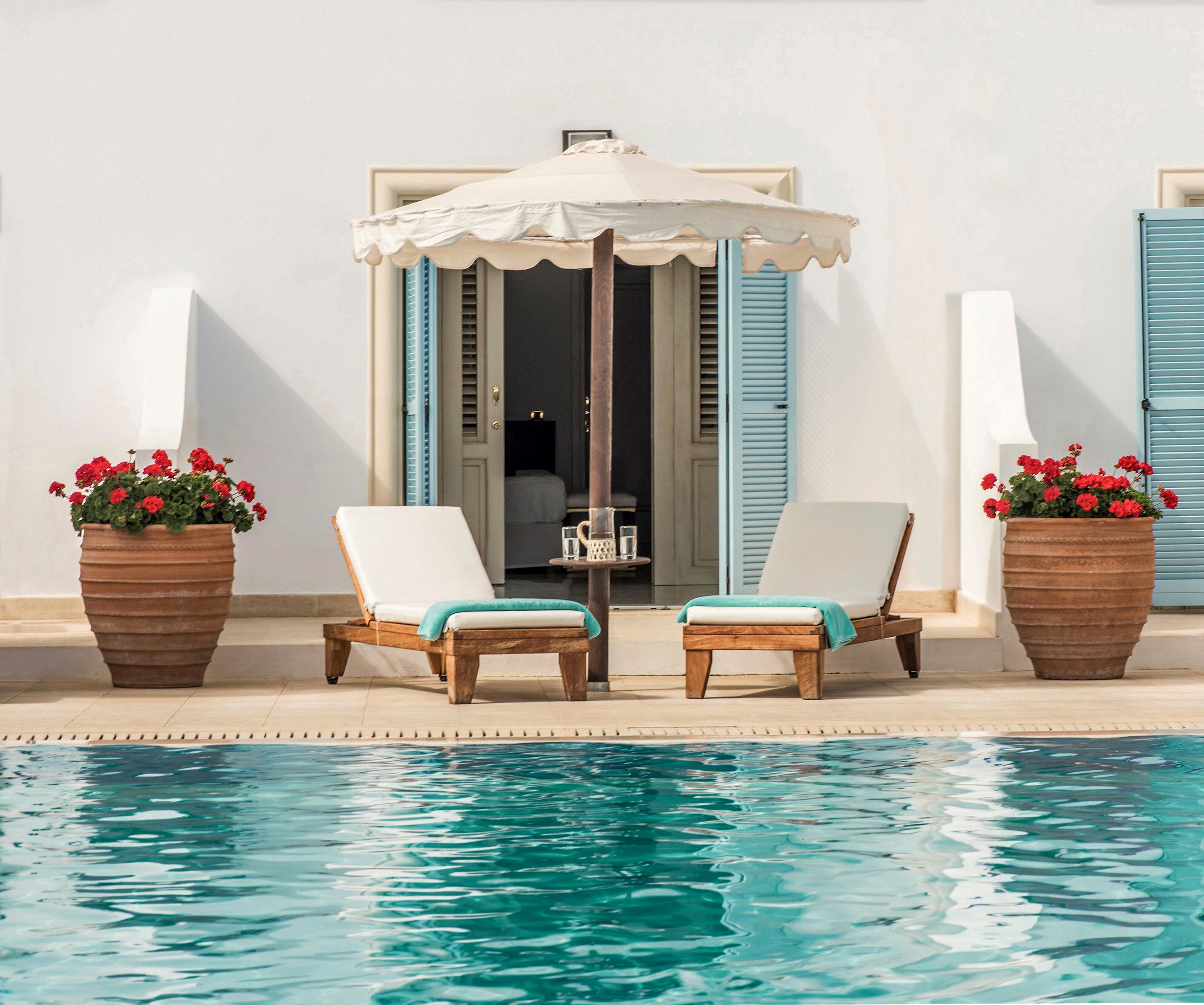 A poolside area with two lounge chairs, a table, and a large umbrella.