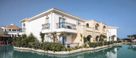 Un edificio grande de dos pisos con piscina delantera, con balcones y arquitectura de piedra.