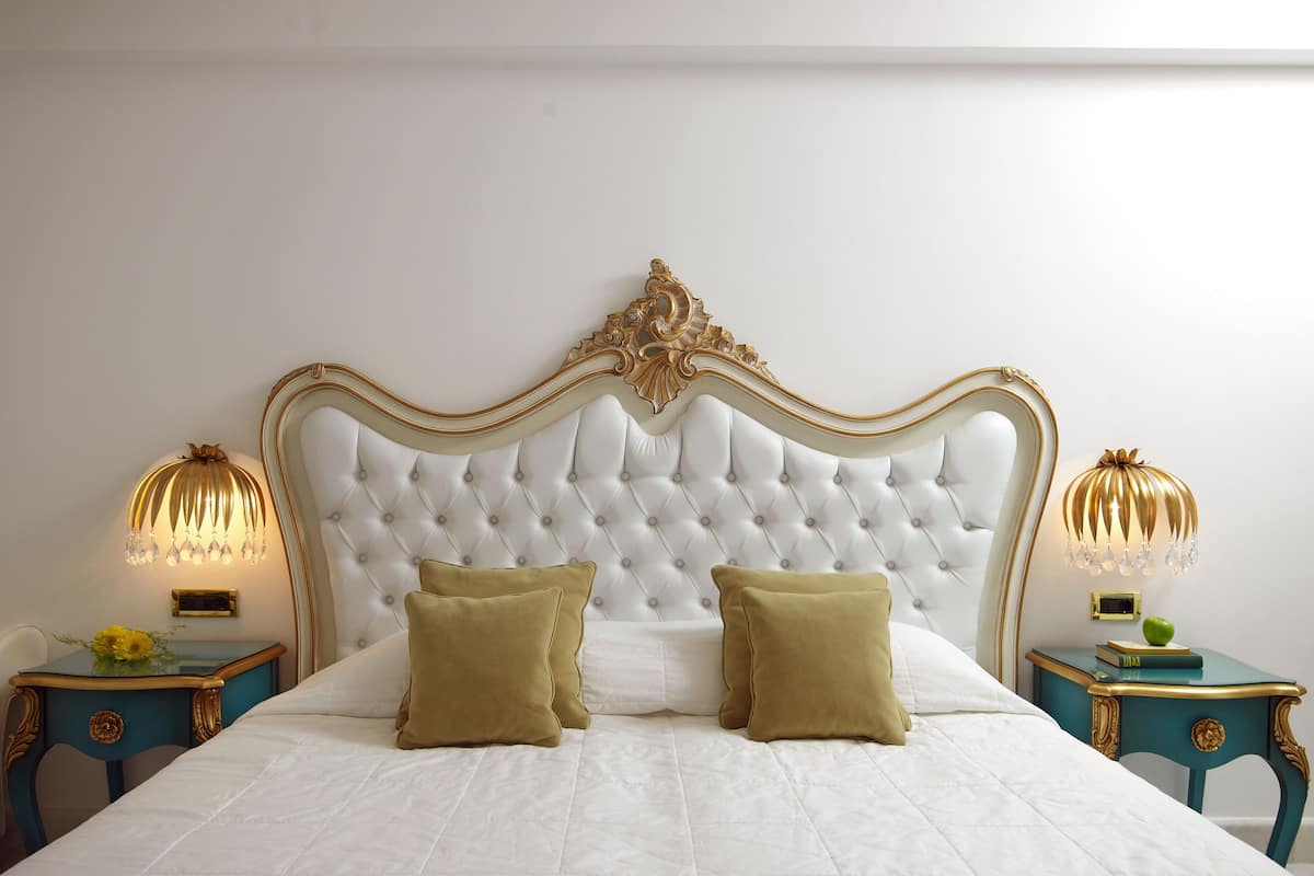Una cama con cabecera capitonada, dos almohadas y dos mesitas de noche con lámparas.