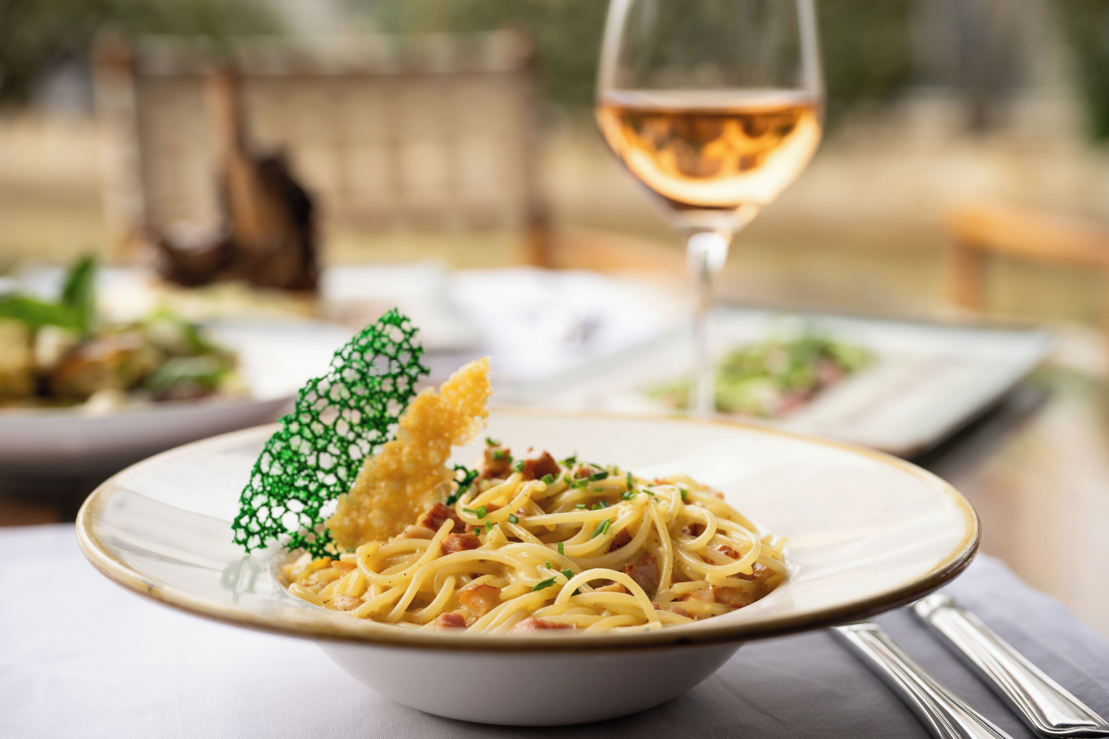 A bowl of pasta with a glass of wine on a table.