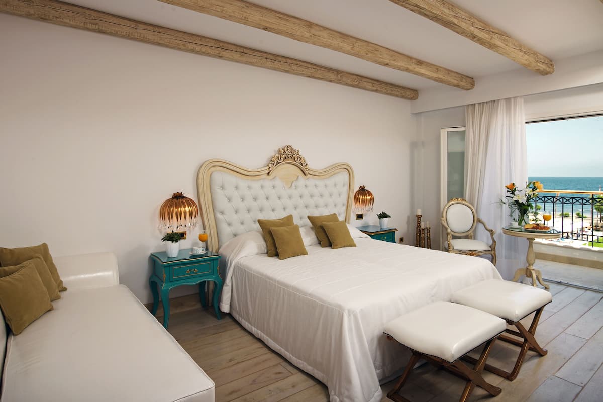 Un dormitorio con una cama grande, un banco, una mesita de noche, un espejo y vista al océano.