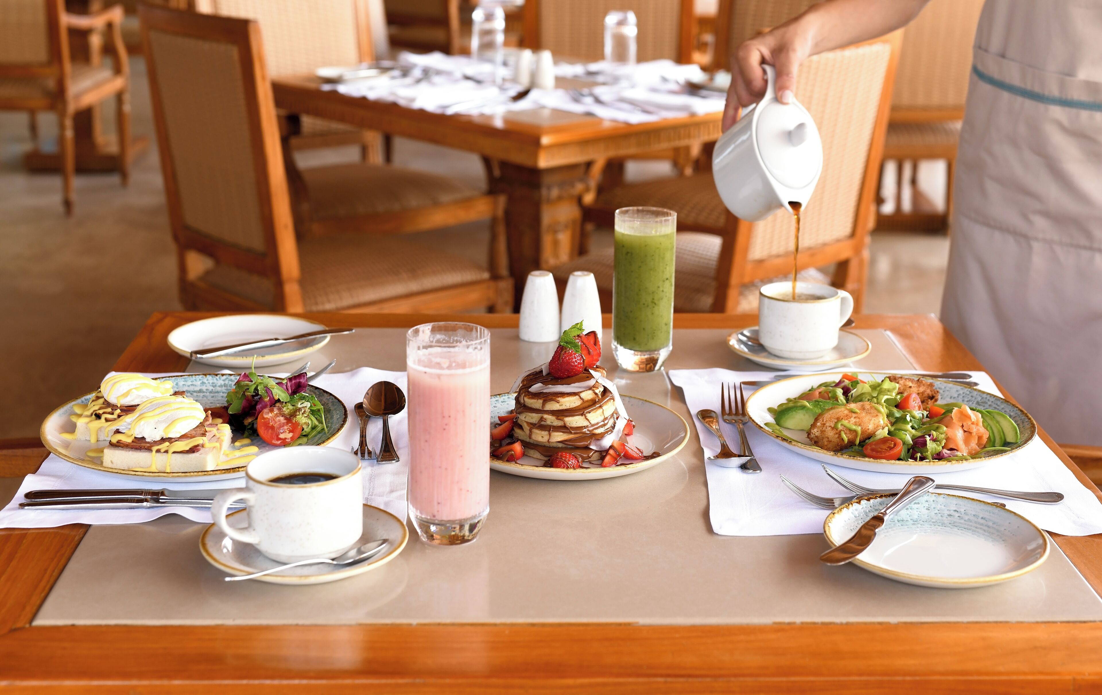 A breakfast setting with various dishes, drinks, and dining utensils on a table.