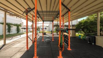 Un gimnasio al aire libre con estructura de metal naranja, discos de pesas y bandas de resistencia.