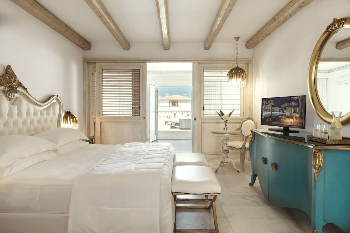 Un dormitorio con una cama grande, un pequeño banco, un escritorio con televisor y un espejo.