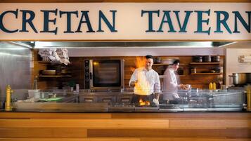 Una cocina con un letrero que dice 'CRETAN TAVERN' y cocineros trabajando.