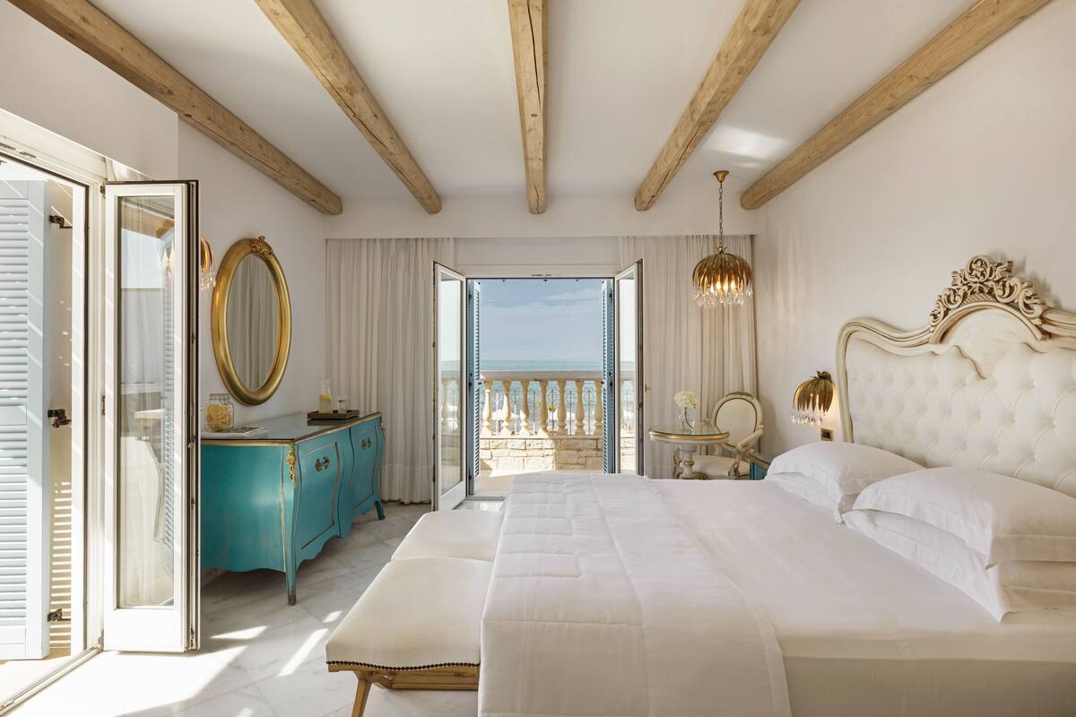 Un dormitorio con una cama grande, techo de madera, balcón con vistas y un aparador azul.
