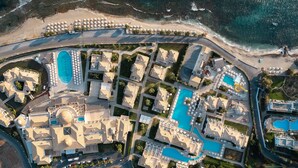 Oversigtsbillede af et resort med flere swimmingpools, en central bygning med kuppel og et strandområde.