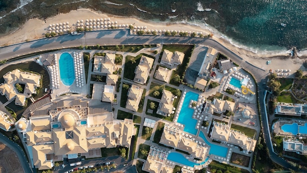 Luftaufnahme eines Resorts mit mehreren Schwimmbecken, einem zentralen Gebäude mit Kuppel und einem Strandbereich.
