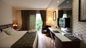 A hotel room with a bed, desk, chair, TV, and a balcony with curtains. - Riva Resatbey Hotel (Adana)