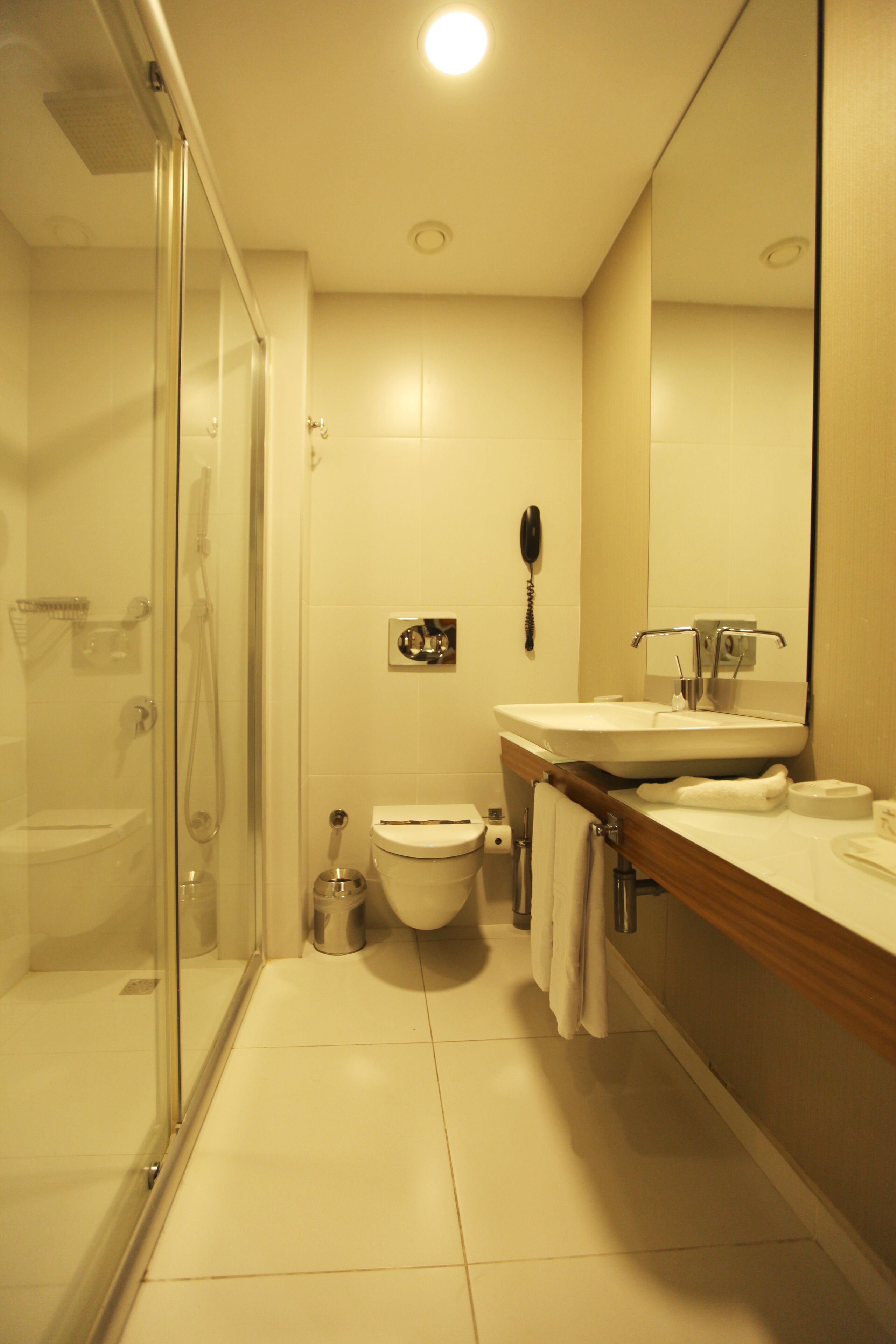 Une salle de bain moderne avec une douche à parois de verre, des toilettes, un lavabo avec un miroir et un téléphone.