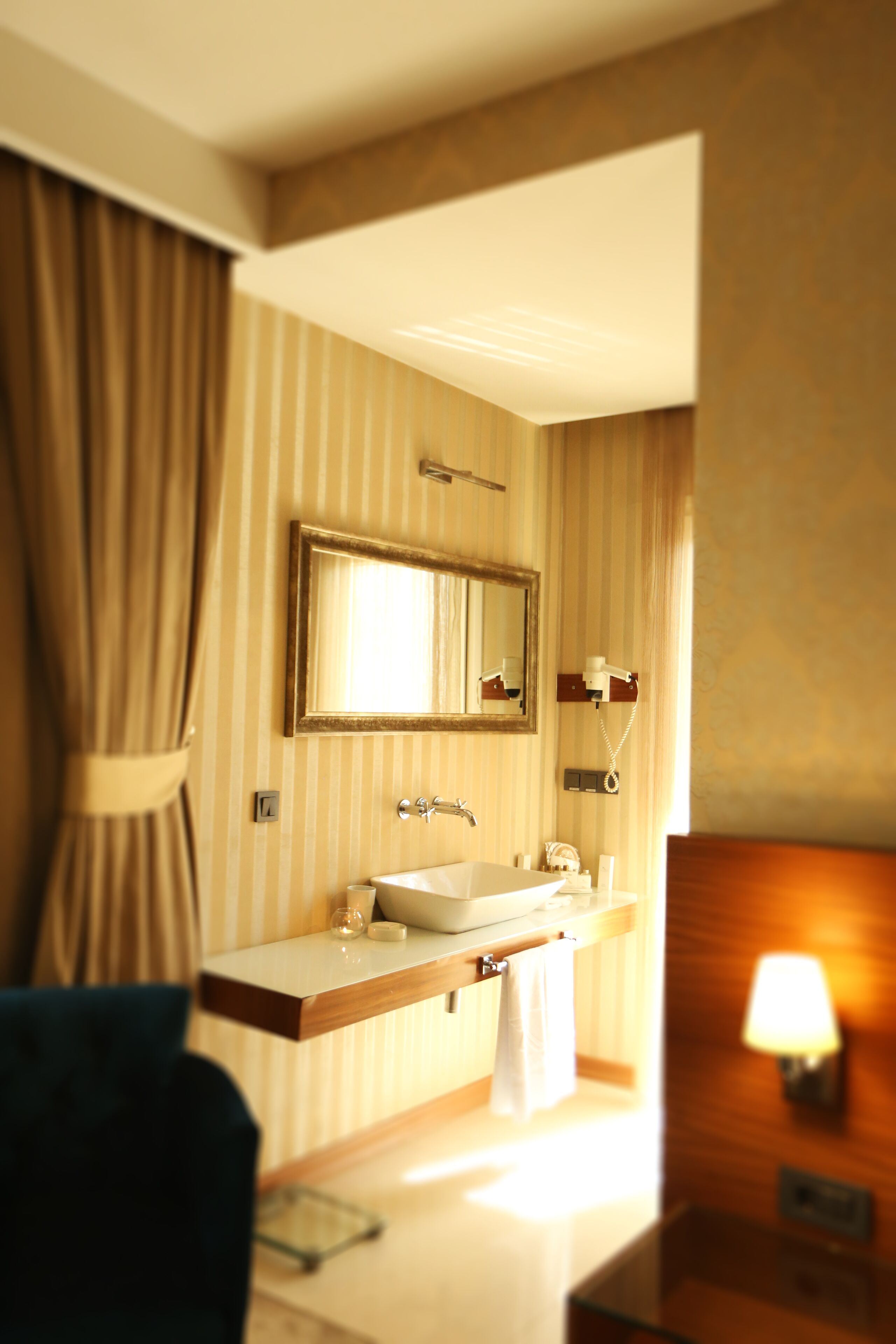 A hotel bathroom with a large mirror, a sink, a towel, and a lamp.