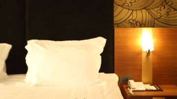 A hotel room with a bed, a tray with cups and a teapot, a nightstand with a lamp, and a patterned wallpaper.