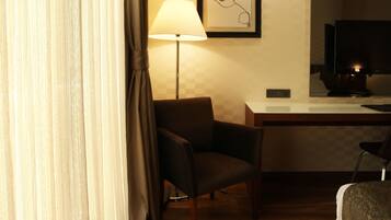 Una habitación de hotel con suelo de madera, un escritorio, una silla, una cama y una lámpara.