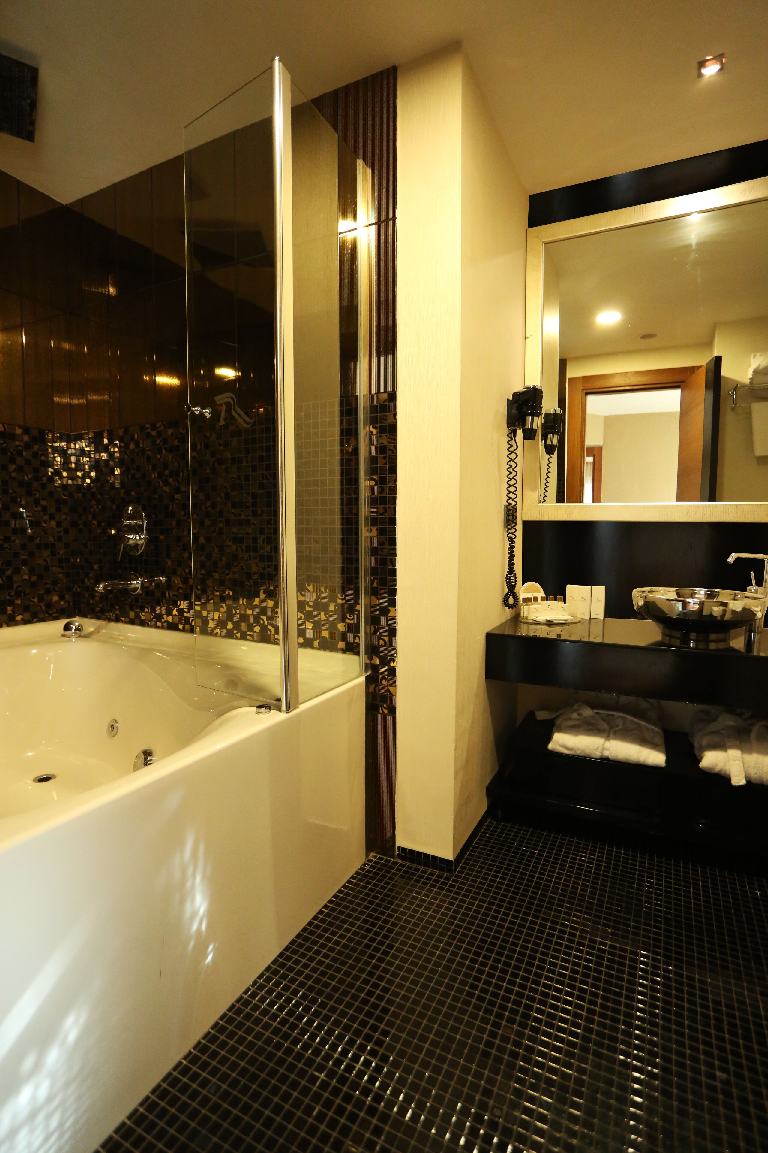 Un baño moderno con ducha de vidrio, una bañera grande y piso de baldosas negras.