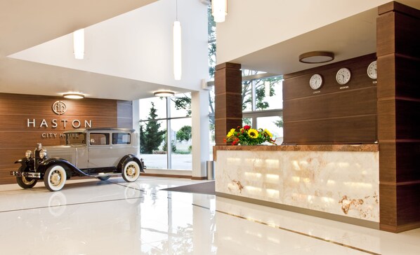 Un moderno vestíbulo de hotel con un coche clásico, un mostrador de recepción y relojes que marcan diferentes zonas horarias.