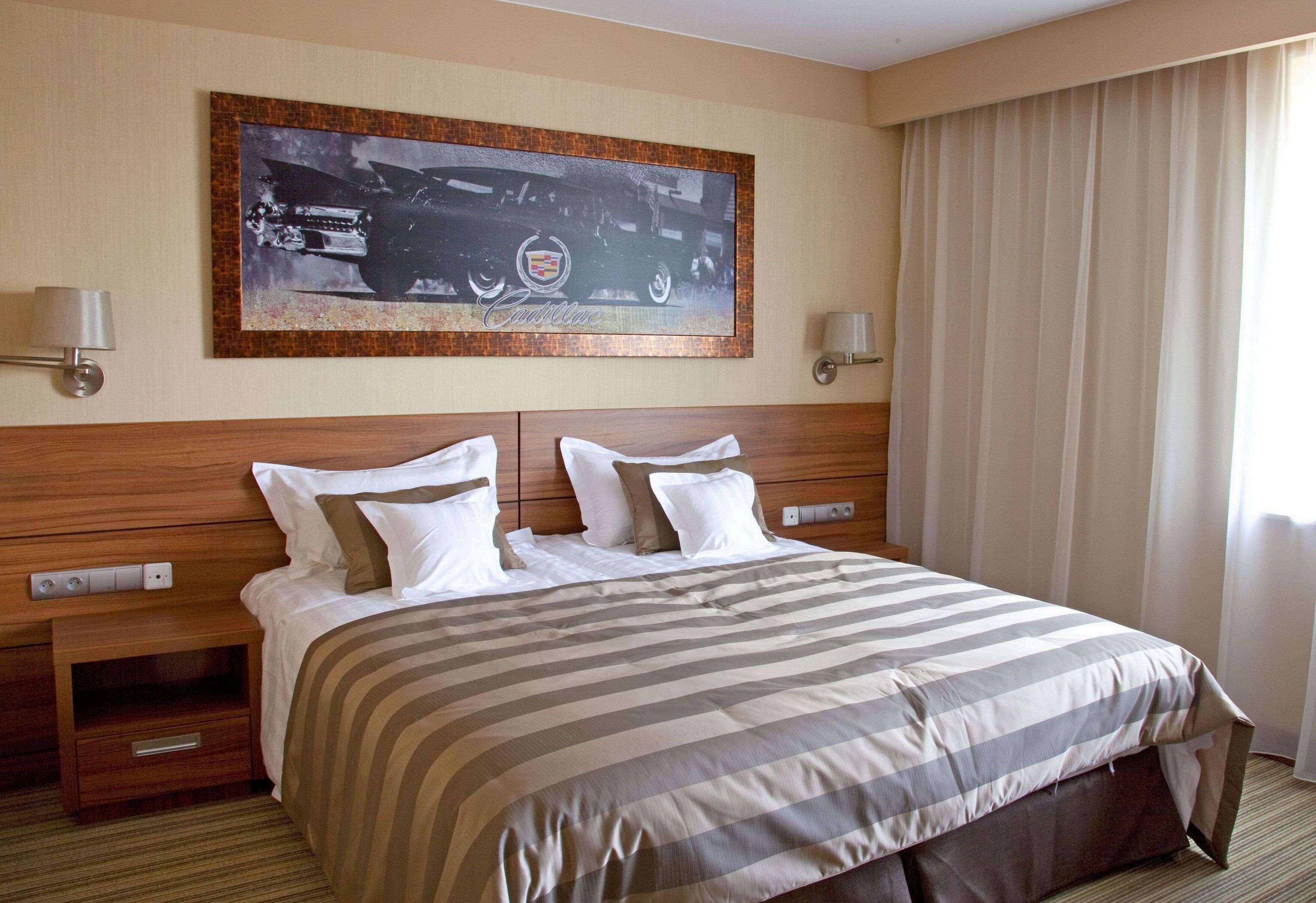 Een hotelkamer met een groot bed, twee nachtkastjes, een aan de muur hangend schilderij en een raam met gordijnen.