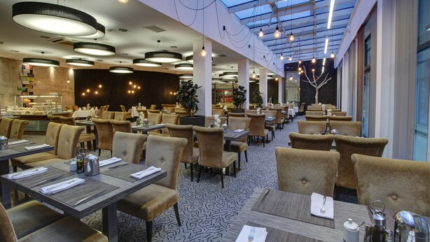 A spacious restaurant with high ceilings, modern lighting, and a central column. Tables are neatly arranged with chairs, and the floor has a patterned design. - Haston City Hotel (Wroclaw)
